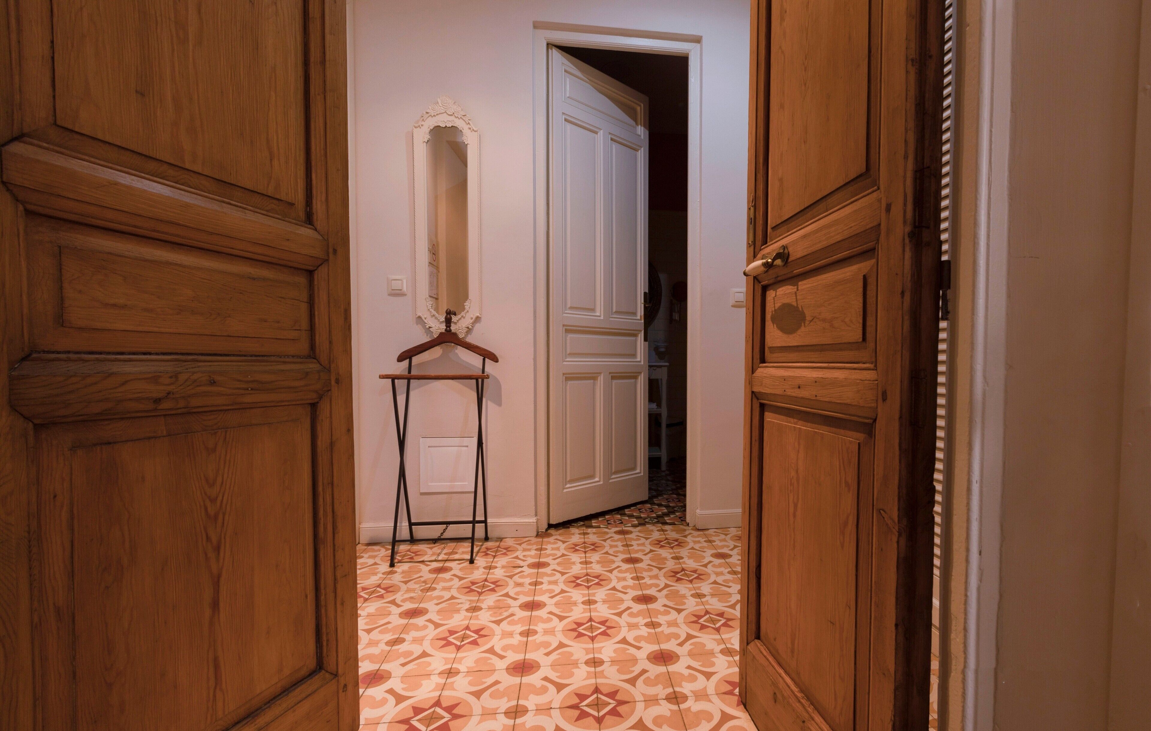 Un couloir avec des portes en bois, un miroir et des carreaux de sol à motifs.