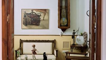 A room with a patterned floor, a wooden bench, a table with a figurine, a clock, and a painting on the wall.