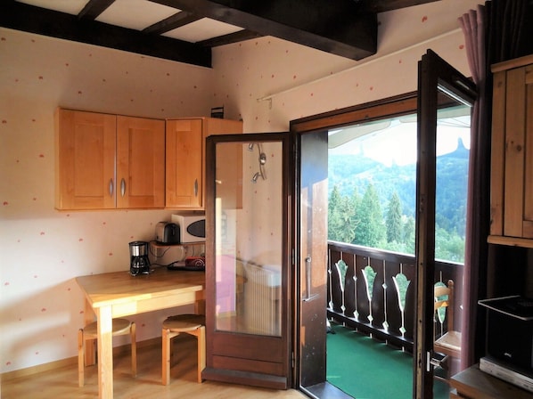 A room with wooden cabinets, a table with a chair, a radiator, and a view of a balcony with a railing.