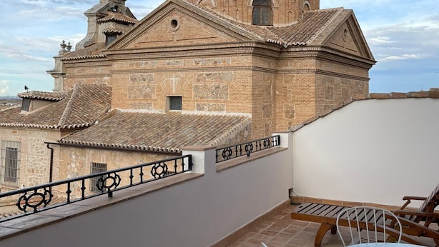 Une terrasse offrant une vue sur un bâtiment historique doté d’un clocher, d’un toit en tuiles et d’une balustrade blanche.