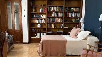 Una habitación con una cama, un sillón mecedora, una estantería y suelo de baldosas.