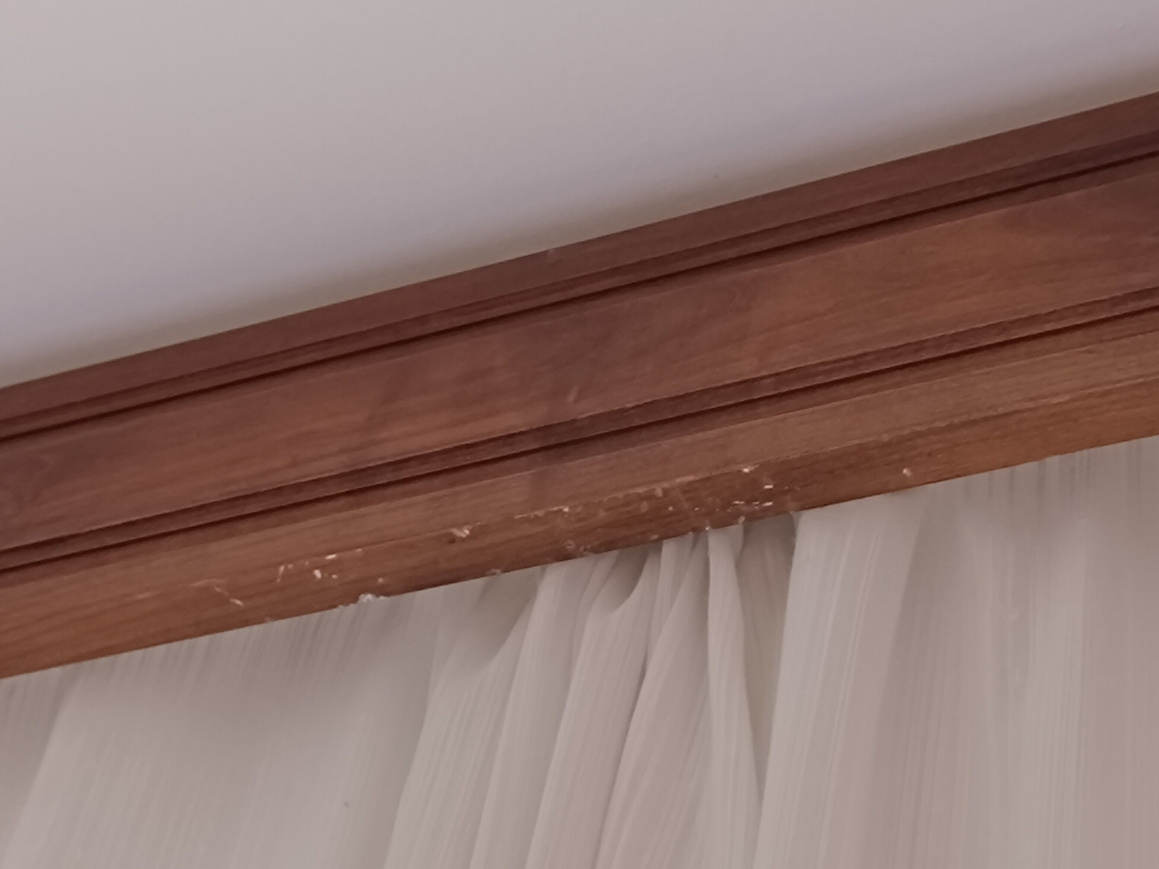 Detalhe de um rodapé de madeira com uma cortina branca.
