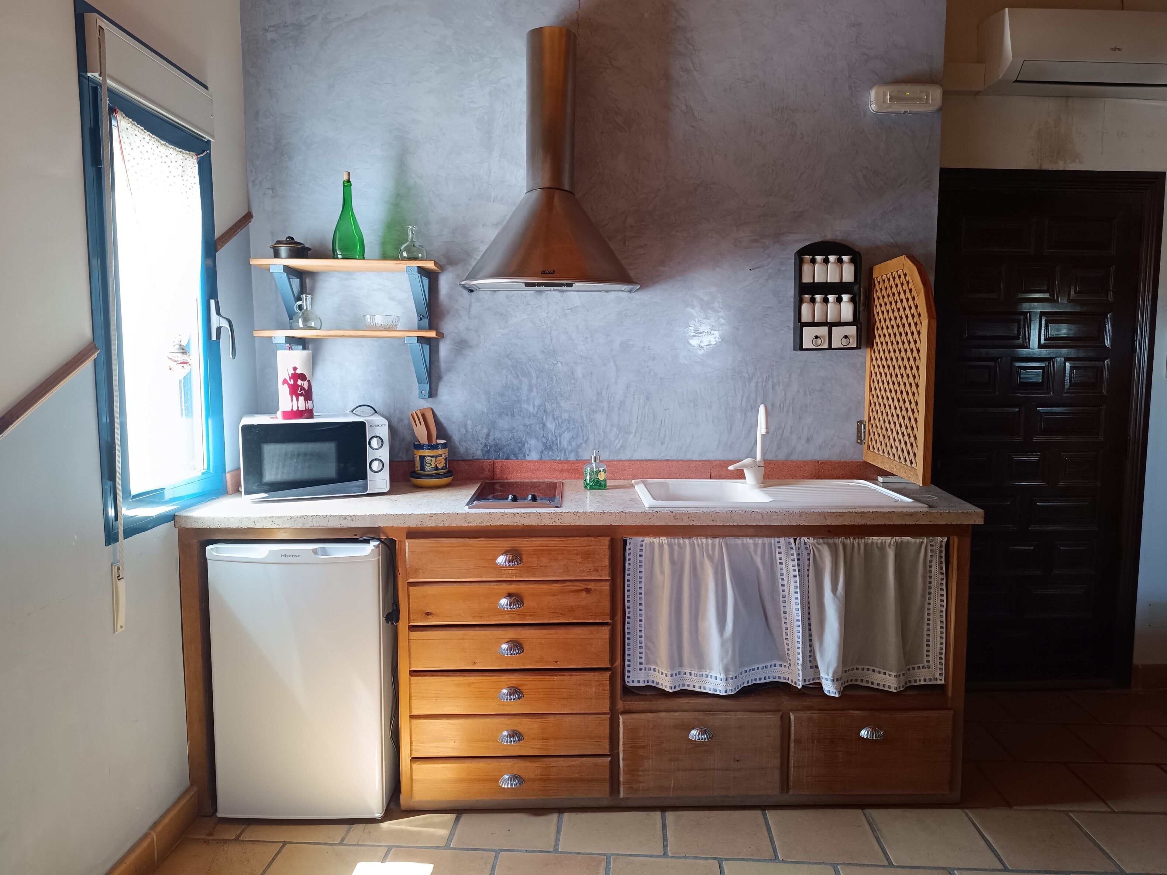 Cozinha compacta com micro-ondas, geladeira, armários de madeira, pia e janela.