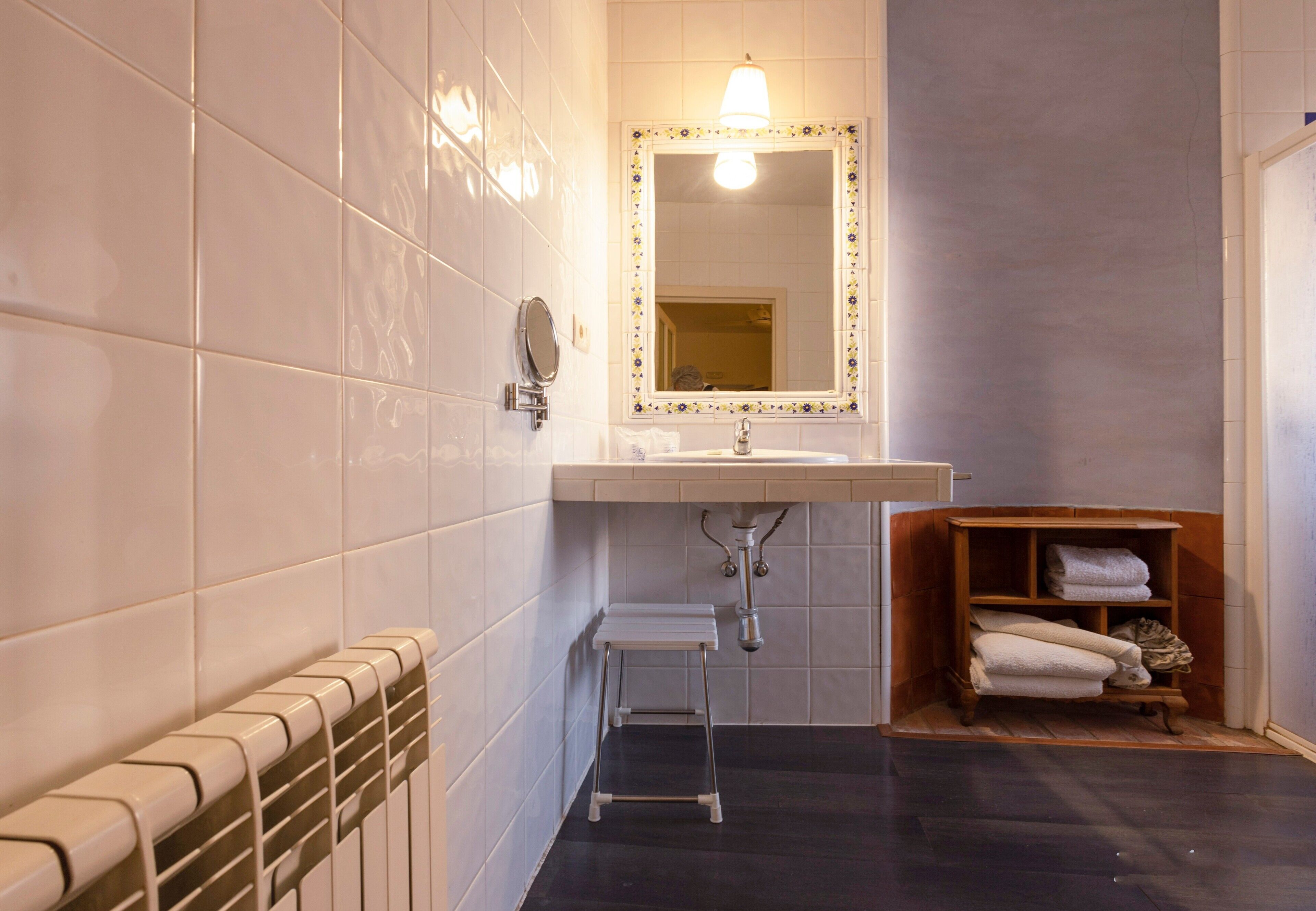 Un baño con un lavamanos blanco, un espejo con marco decorativo, un taburete pequeño y un estante de madera con toallas.