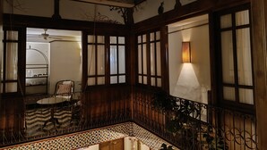 A room with a wooden balcony, a ceiling fan, a table with chairs, and a wall-mounted lamp. - Family Room La Hornacina, Hotel Rural Consuegra (Consuegra)