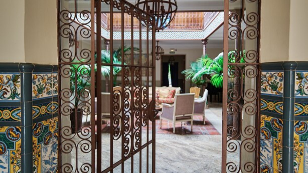 An arched entrance with decorative metalwork, a tiled floor, and a seating area with chairs and a table. - Family Room La Hornacina, Hotel Rural Consuegra (Consuegra)