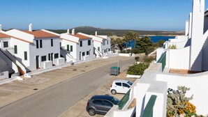 A coastal street with white buildings, a parked car, and a clear view of the sea. - Gin & Tonic Apartment in Son Parc with Pool, Padel Court, and Sea View near Son Saura Beach (Son Parc)