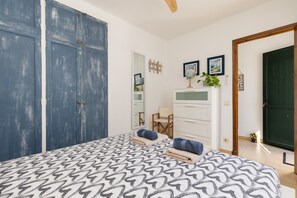 A bedroom with a patterned bedspread, a dresser, a chair, a mirror, and a door.