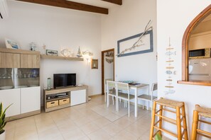 A modern kitchen with white cabinetry, a TV, and a dining area with a white table and chairs.