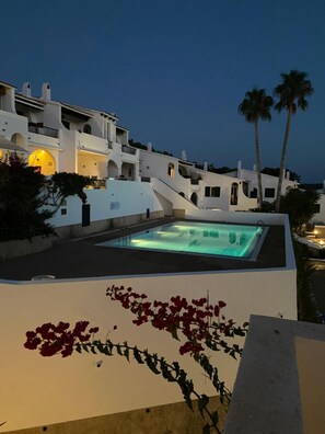 A rooftop pool with a modern design, surrounded by white buildings with balconies and palm trees.