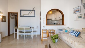 A living room with a sofa, chairs, a dining table, a kitchen visible through an archway, and wall decorations. - Gin & Tonic Apartment in Son Parc with Pool, Padel Court, and Sea View near Son Saura Beach (Son Parc)