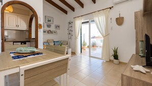 A modern kitchen with wooden beams, a dining area with a table and chairs, a sofa, and a TV. - Gin & Tonic Apartment in Son Parc with Pool, Padel Court, and Sea View near Son Saura Beach (Son Parc)