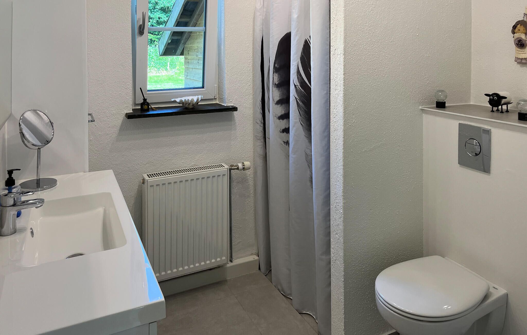 Ett badrum med ett vitt handfat, en spegel, en toalett och ett element.