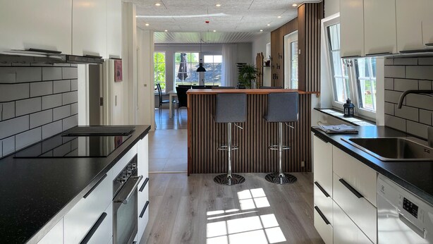 Uma cozinha moderna com uma ilha central, banquetes altos e vista para uma sala de jantar.