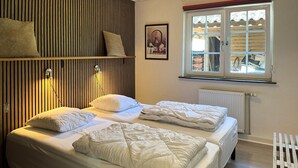 Quarto com cama, janela, radiador e parede de ripas de madeira.