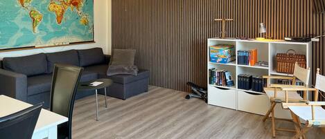 Een woonkamer met een grote wereldkaart, een bank, een salontafel, een boekenkast en een bureau met een stoel.