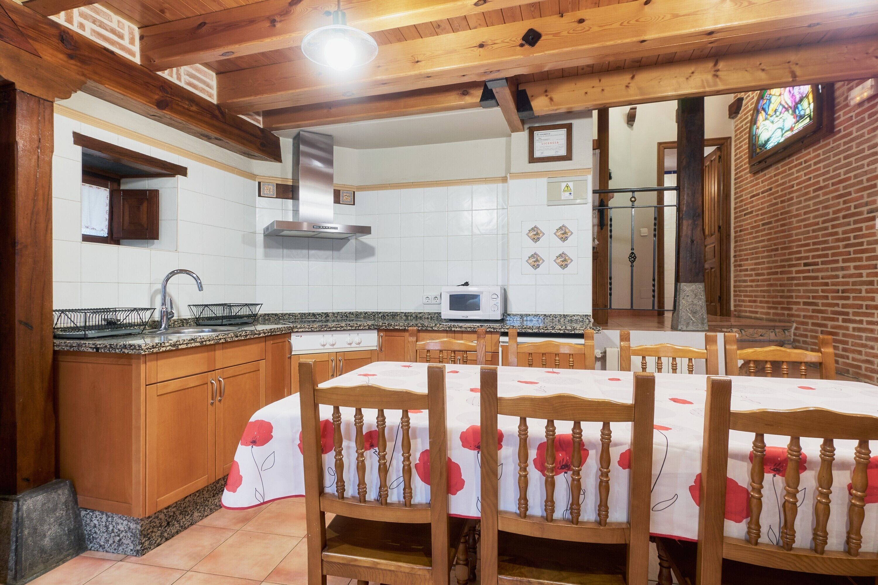 Una cocina con armarios de madera, microondas y comedor con sillas y mesa.