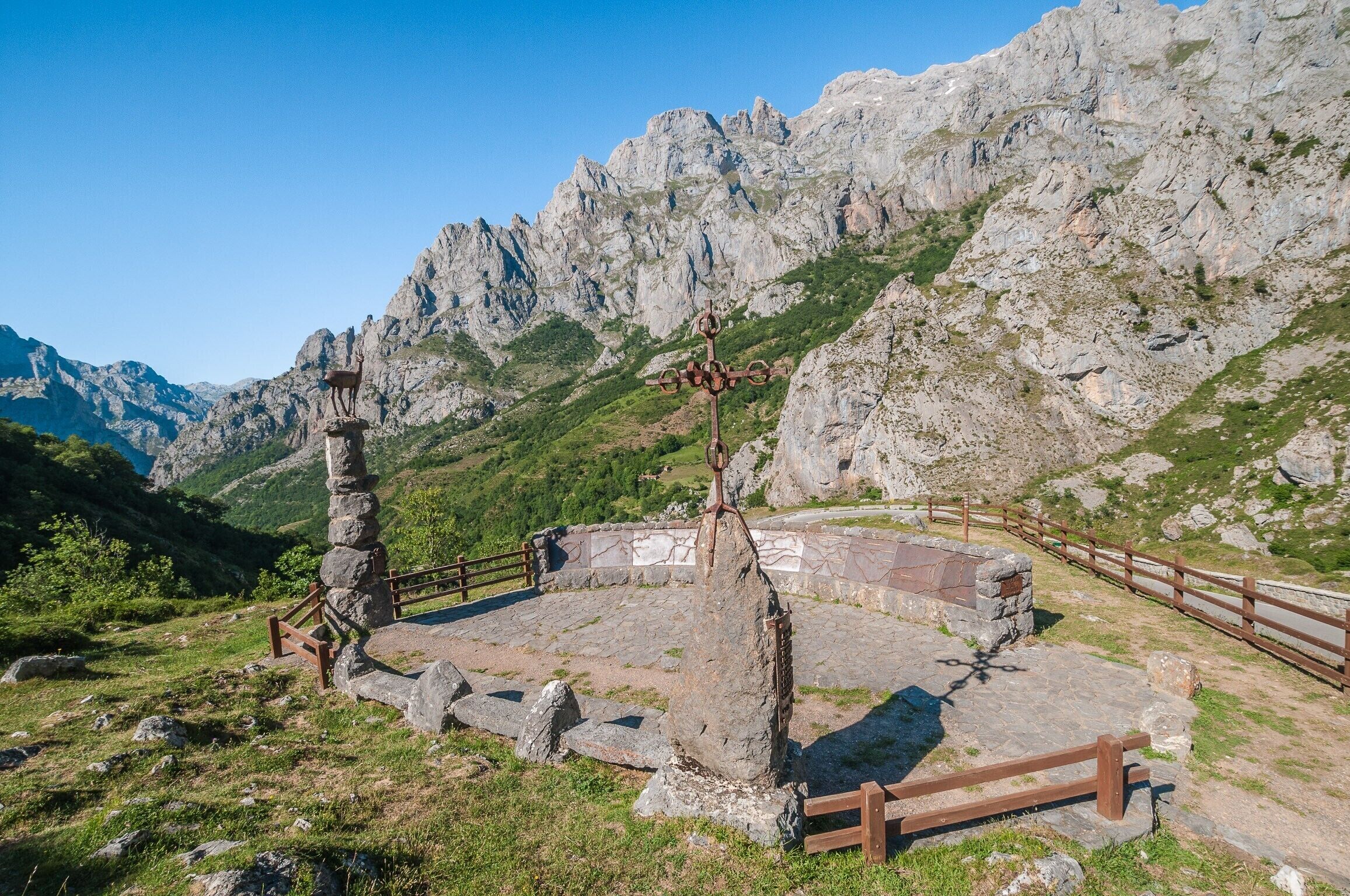 Una edificación de piedra con un cerco de madera, rodeada de terreno pedregoso y montañas.