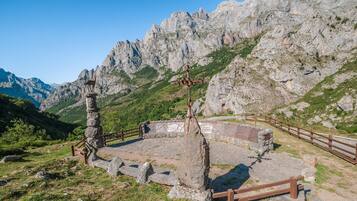 Una edificación de piedra con un cerco de madera, rodeada de terreno pedregoso y montañas.