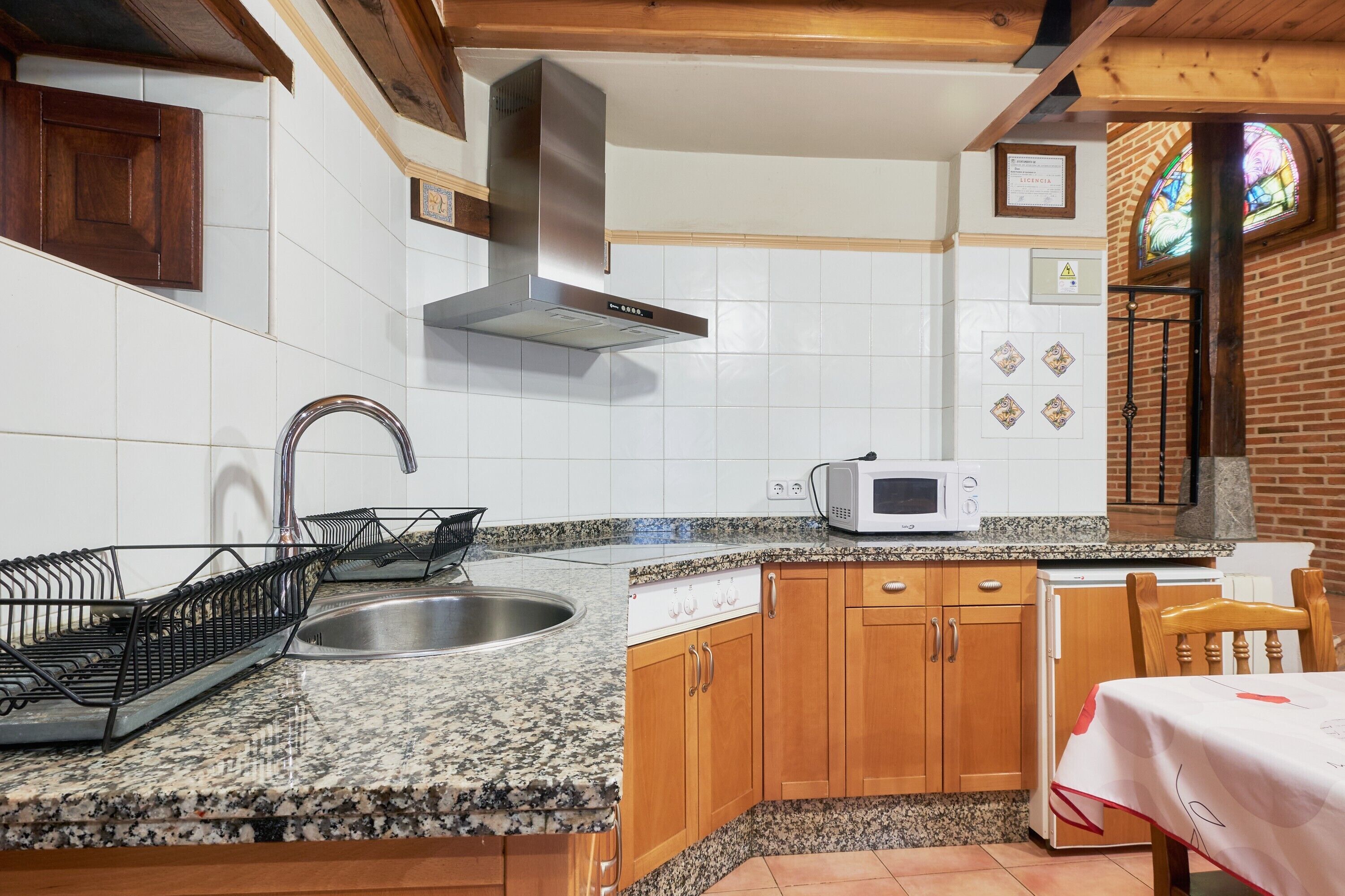 Una cocina con encimeras de granito, armarios de madera, un lavamanos de acero inoxidable, un microondas y una estufa.