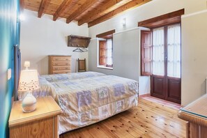 A bedroom with a bed, wooden floor, dresser, lamp, and a window with curtains. - Country House 'El Serenal' with Mountain View, Private Terrace and Wi-Fi (Santa Marina de Valdeón)