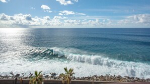 A coastal view with waves, a clear sky, and a rocky shoreline.