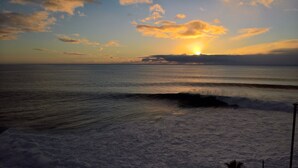 Een strand met golven en een ondergaande zon.