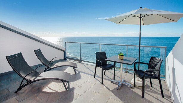 Een balkon met een tafel, stoelen en een parasol, met uitzicht op zee.