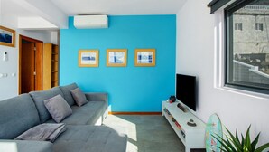 Uma sala de estar moderna com uma parede azul de destaque, um sofá cinza, uma televisão de tela plana e uma decoração com prancha de surf.