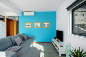 Een moderne woonkamer met een blauwe accentmuur, een grijze bank, een flatscreen televisie en een decoratieve surfboard.