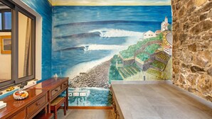 Quarto com um mural de paisagem costeira, uma escrivaninha de madeira e uma parede de pedra.
