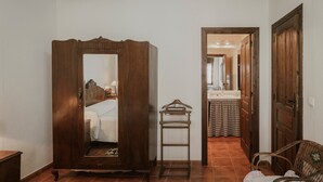 A room with a wooden wardrobe, a mirror, a chair, and a view into a bathroom.