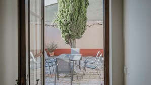 Une porte ouverte donnant sur un patio extérieur, avec une table et des chaises, un pot de fleurs et un mur.