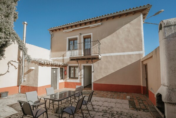 A two-story building with a balcony, a patio with a table and chairs, and a tiled floor.