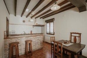 A kitchen with a brick island, wooden stools, a dining table with chairs, and a hanging light fixture.