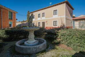 A courtyard with a fountain, a statue, and a building with multiple windows and a door.