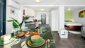 A modern kitchen with white cabinets, a stainless steel refrigerator, and a dining area with a glass table set for four. - Apartment 'The Wave House - Seaside Haven' with Sea View, Wi-Fi and Air Conditioning (Jardim do Mar)