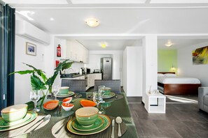 A modern kitchen with white cabinets, a stainless steel refrigerator, and a dining area with a glass table set for four. - Apartment 'The Wave House - Seaside Haven' with Sea View, Wi-Fi and Air Conditioning (Jardim do Mar)