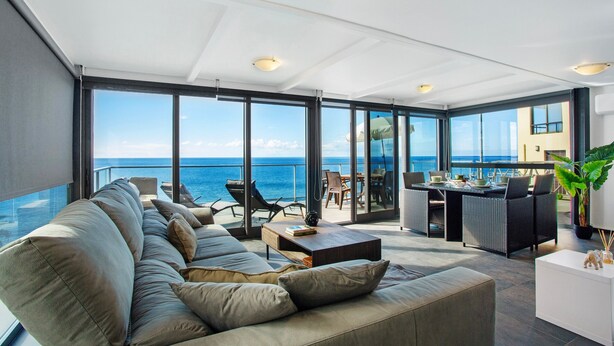 A modern living room with a large sofa, a coffee table, and a dining area with chairs and a table. - Apartment 'The Wave House - Seaside Haven' with Sea View, Wi-Fi and Air Conditioning (Jardim do Mar)