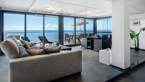 A spacious living area with a large window overlooking the sea, a sofa, dining area, and a small table with decorative items. - Apartment 'The Wave House - Seaside Haven' with Sea View, Wi-Fi and Air Conditioning (Jardim do Mar)