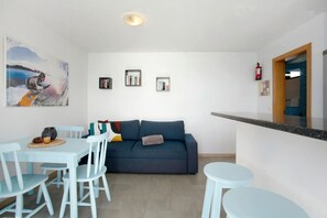 A modern living room with a sofa, dining table, chairs, and a small kitchen area with a counter.