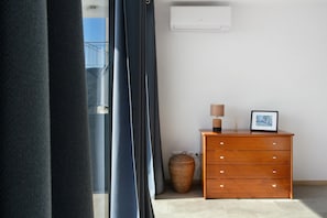 A room with a wooden dresser, a lamp, a picture frame, a wicker basket, and a wall-mounted air conditioner.