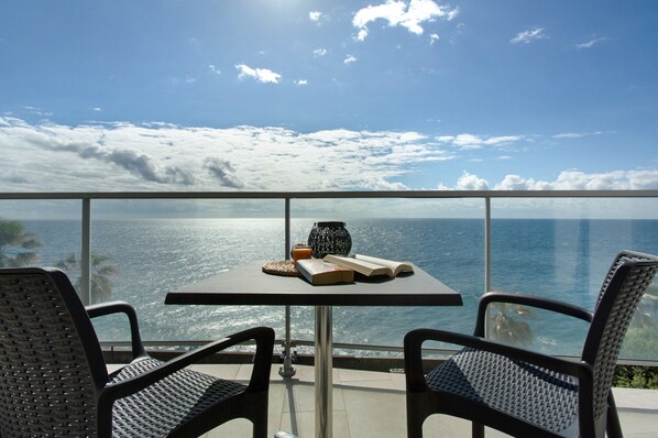 A balcony with a table, two chairs, a book, a vase, and a glass of orange juice.
