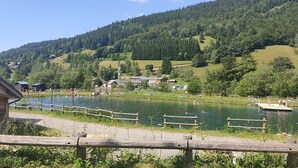 A lakeside view with a wooden dock, a small wooden building, and a forested hillside in the background. - Studio 'Grand Serre' with Lake View and Private Terrace (La Morte)