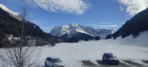A snowy mountain landscape with a clear sky, a few buildings, and two parked cars.