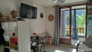 A living room with a TV, a dining area with a table and chairs, a sofa, and a balcony with a view. - Studio 'Grand Serre' with Lake View and Private Terrace (La Morte)