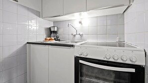 Une cuisine de taille réduite, avec des meubles blancs, une machine à café, un évier et un four.