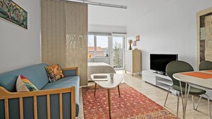 Un salon moderne comprenant un canapé, un téléviseur, un coin repas et une vue dégagée sur l’extérieur grâce à une grande fenêtre.