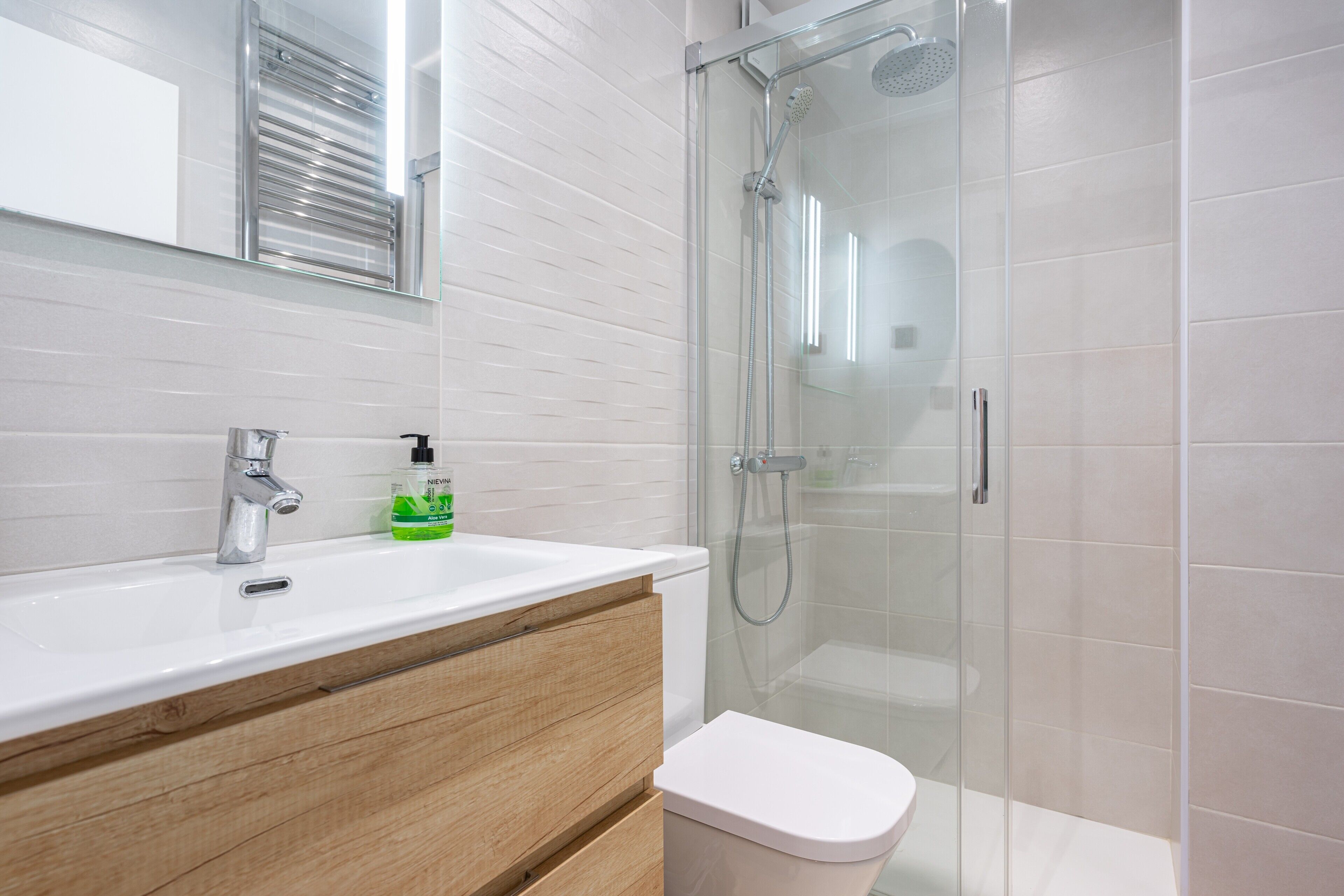 A modern bathroom with a glass-enclosed shower, a white sink, and a wooden vanity.