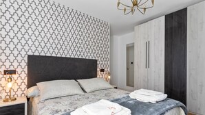 A modern bedroom with a patterned wall, a large bed with pillows, a nightstand with a lamp, and a wardrobe. - Apartment 'Comarca Del Sella' with Mountain View and Wi-Fi (Arriondas)
